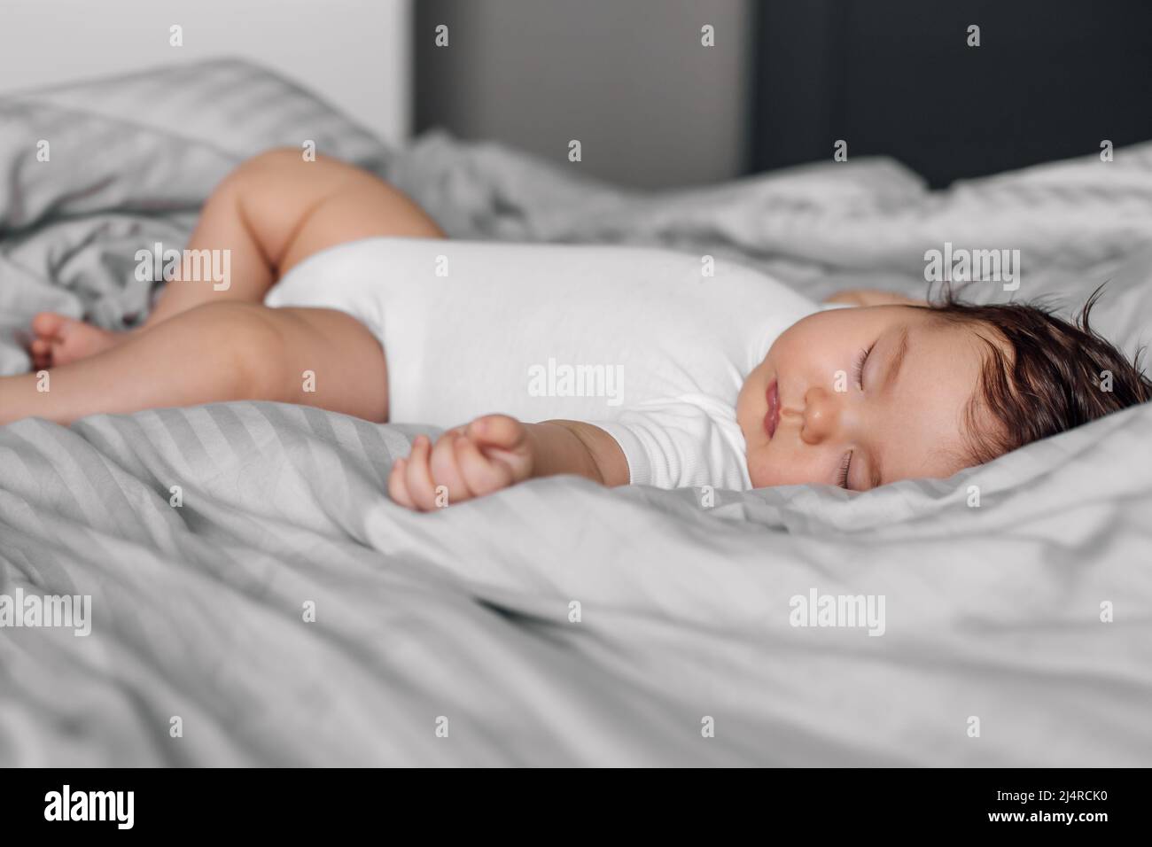 Portrait eines Babys im Schlaf Body, der auf der Decke auf dem Bett liegt. Schlafende Kleinkind im Schlafzimmer, siehe süßen Traum. Grauer Hintergrund, weicher Fokus, freie Kopie Stockfoto