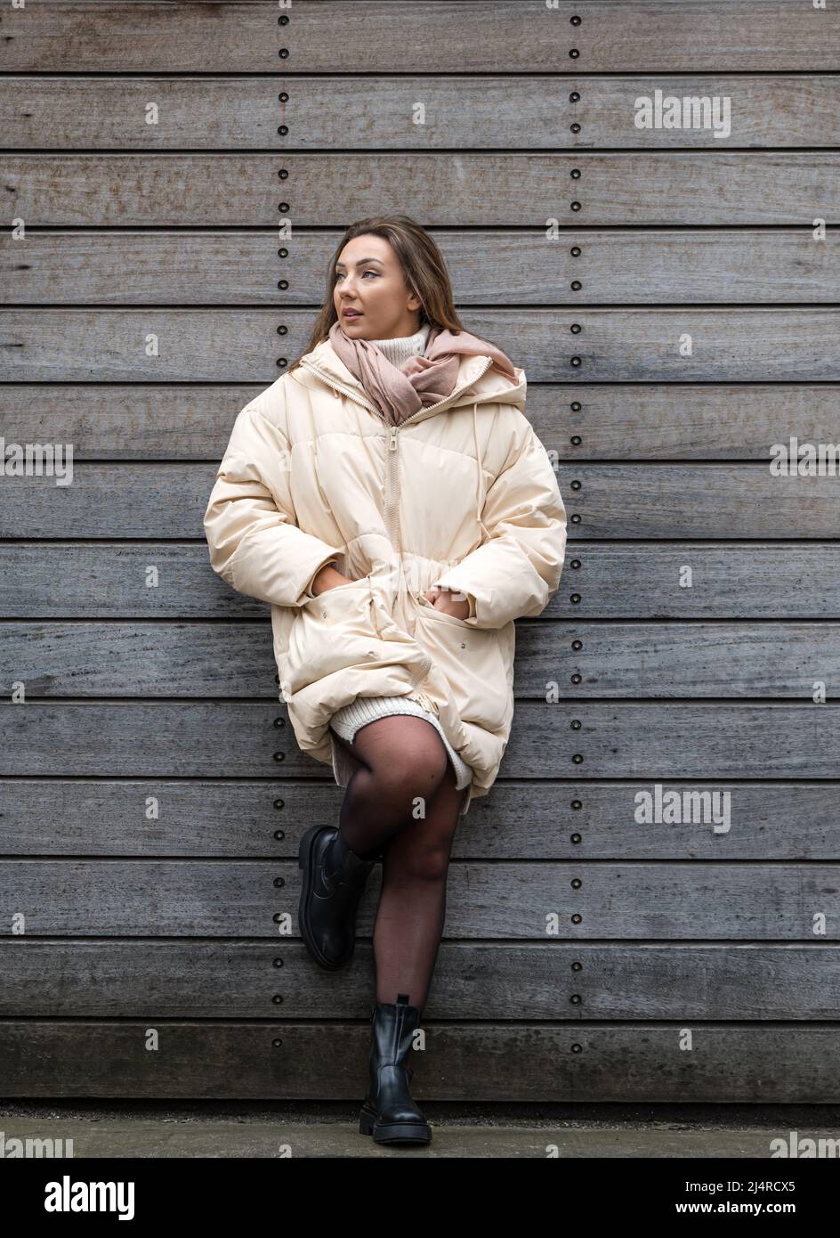 Eine hübsche junge Frau oder ein Model, die eine Winterjacke an einer Wand trägt, Edinburgh, Schottland, Großbritannien Stockfoto