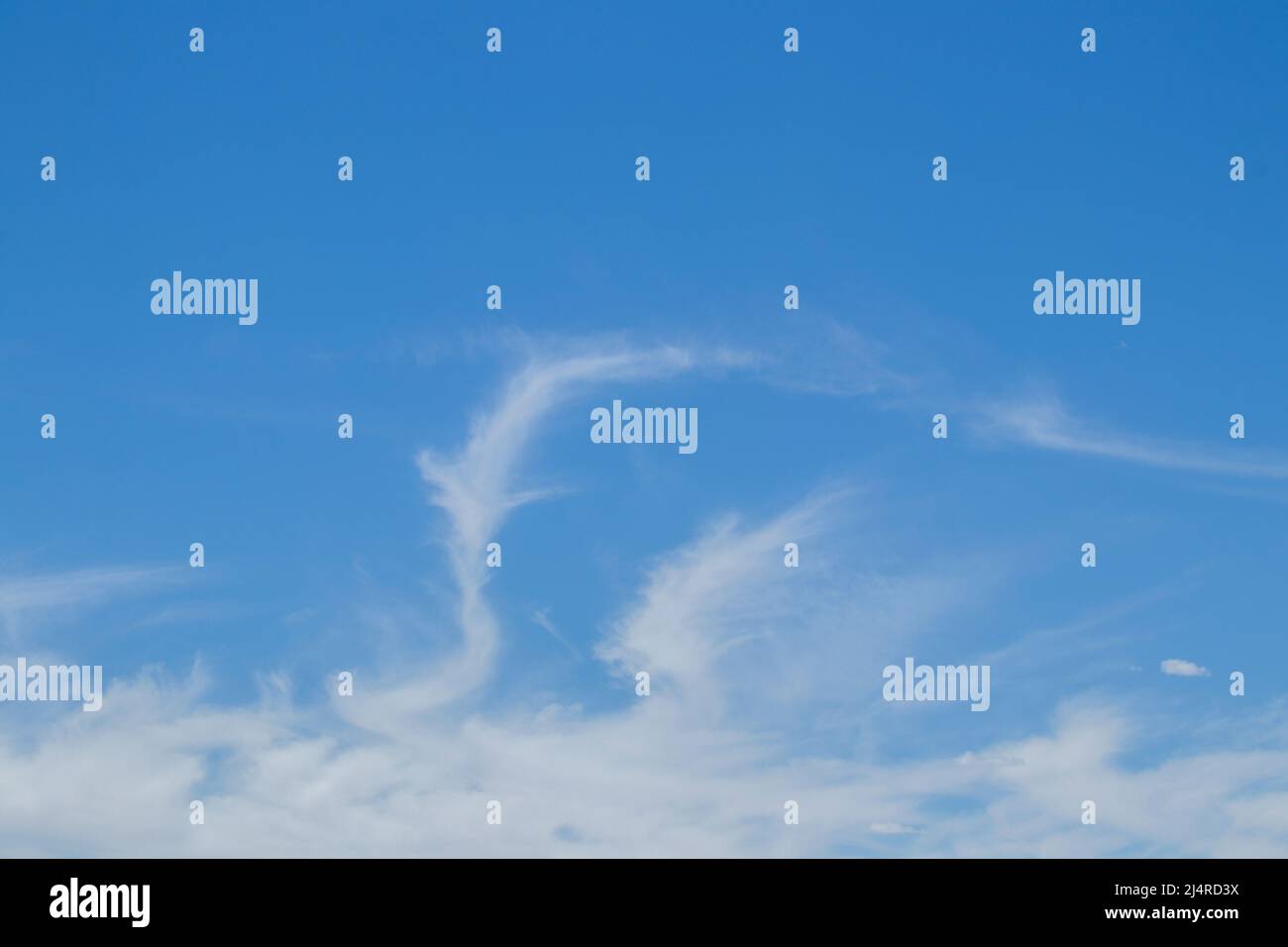 Blauer Himmel mit weißen Wolken unten und einem Wolkenwirbel, der sich in den Himmel einreibt - Hintergrund oder Versetzung. Stockfoto