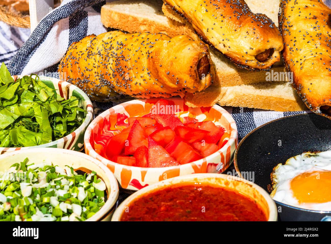 Rustikale Zusammensetzung mit Würstchenbrötchen und verschiedenen Schüsseln mit Sauce und gehacktem Gemüse (Tomaten, grüner Salat, grüne Zwiebel, grüner Knoblauch) Stockfoto