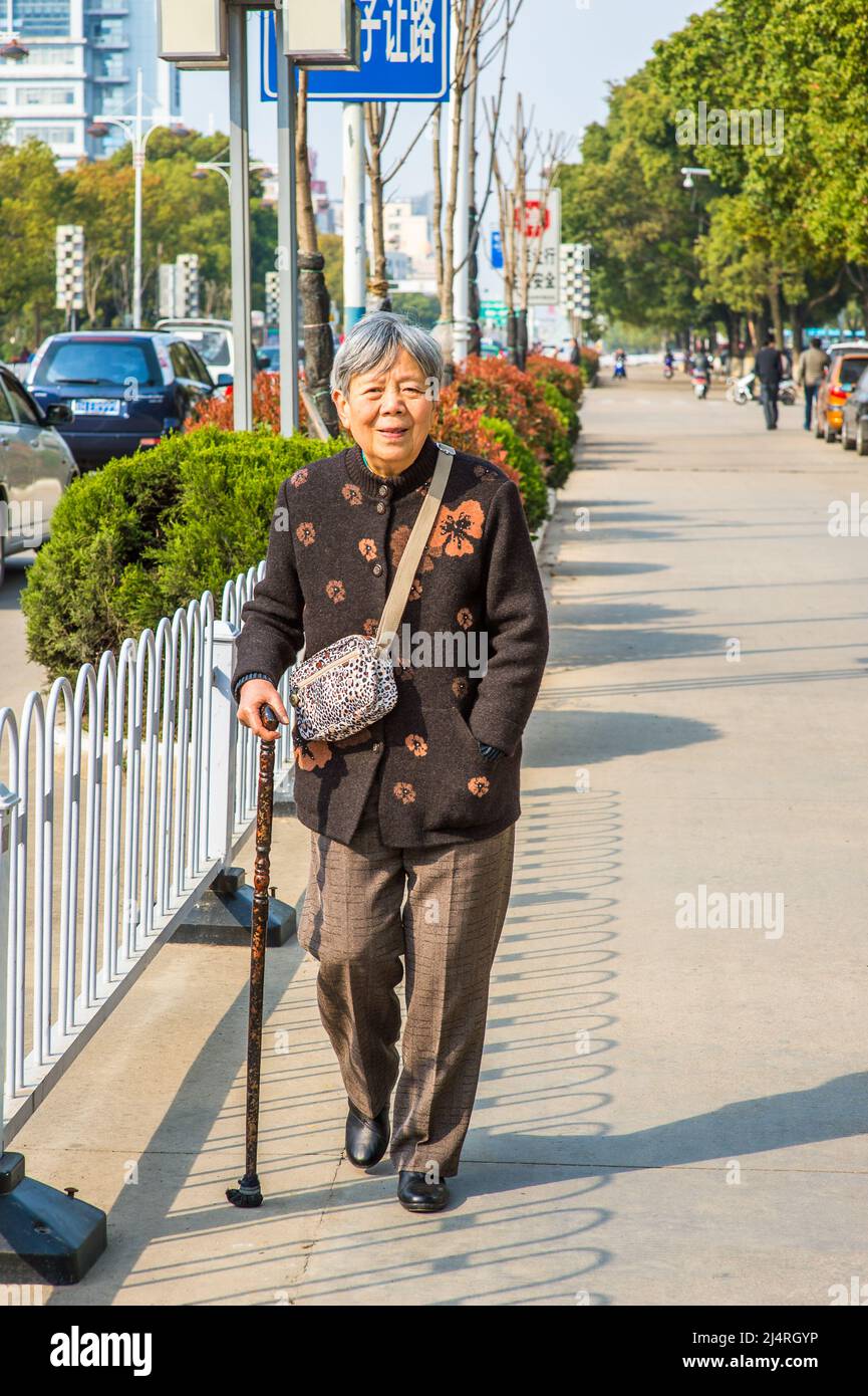 ANQING, CHINA - 21. MÄRZ: Ältere Frau geht auf der Straße. Am 21. März 2014 spaziert eine 80 Jahre alte chinesische Dame mit einem Stock auf der Straße. Stockfoto