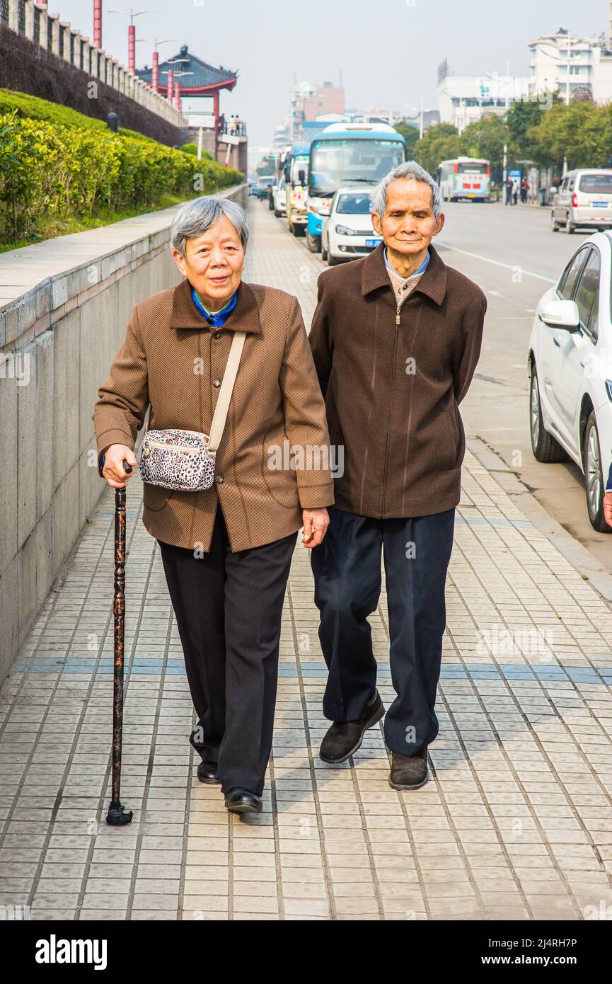 Ältere Männer und Frauen, die nach draußen gehen. Ein älteres Paar, 80 Jahre alt, geht auf der Straße, eine Frau hält einen Spazierstock. Stockfoto