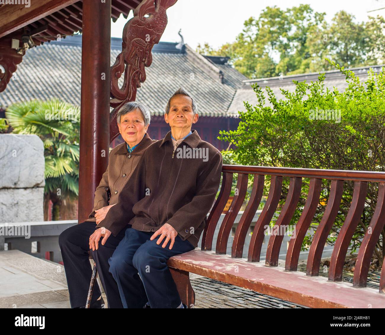 Ältere Männer und Frauen sitzen auf einer langen Bank, um eine Pause zu machen. Ein älteres Paar, 80 Jahre alt, sitzt auf einer Bank in einem buddhistischen Tempel, während es sich sieht Stockfoto