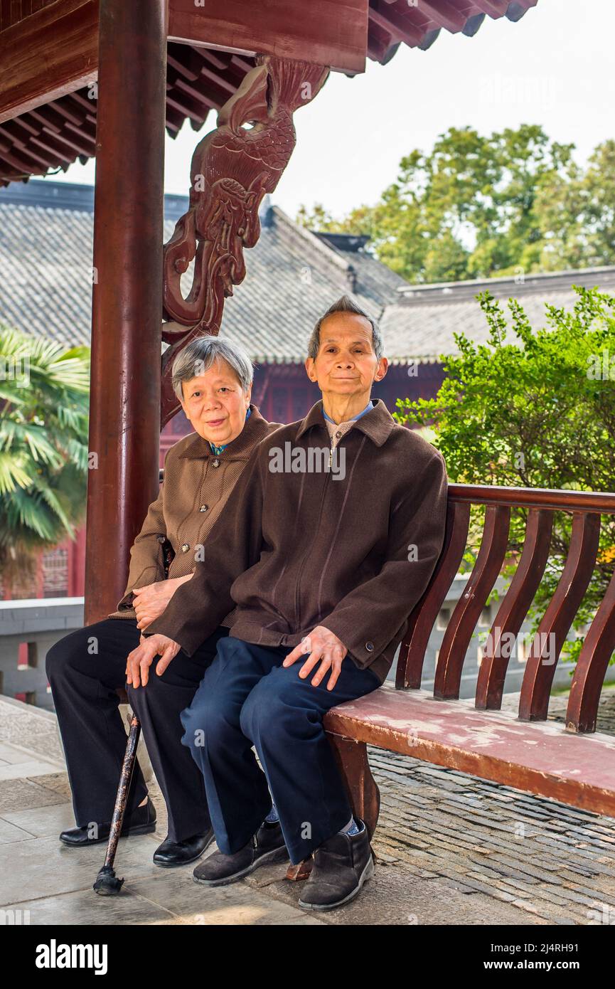 Ältere Männer und Frauen sitzen auf einer langen Bank, um eine Pause zu machen. Ein älteres Paar, 80 Jahre alt, sitzt auf einer Bank in einem buddhistischen Tempel, während es sich sieht Stockfoto
