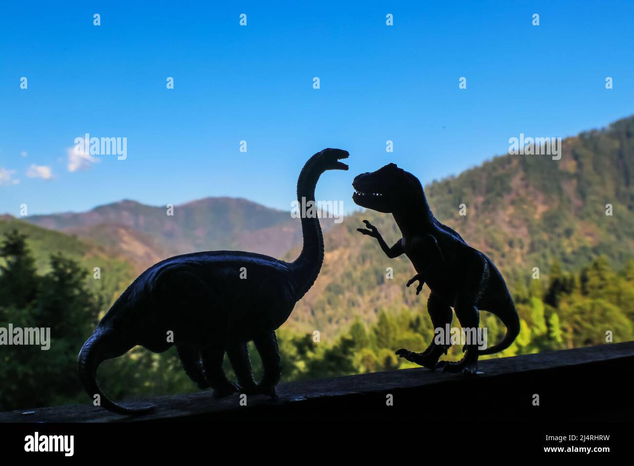 Zwei Dinosaurier - ein Brontosaurus und ein t rex - konfrontieren sich in Silhouette mit unscharf abgeschnittenen Bergen in der Ferne Stockfoto