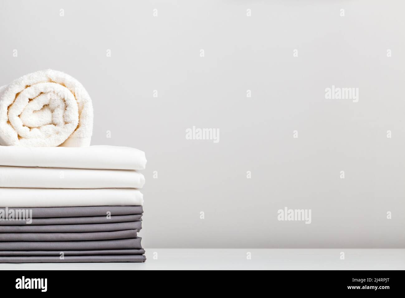 Ein Stapel grauer und weißer Bettwäsche, Laken und ein Frottee-Handtuch auf dem Tisch. Stockfoto