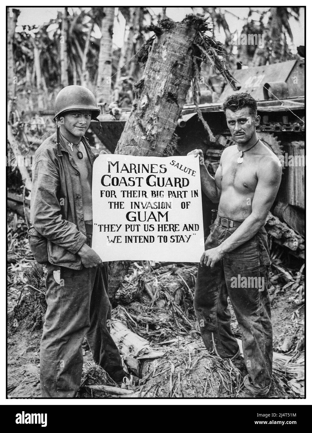 WW2 Guam 1944 die US-Marine grüßt die US-Küstenwache, nachdem die Wut der Schlacht nachgelassen und die Japaner auf Guam besiegt worden waren. „Sie (die Küstenwache) haben uns hierher gebracht und wir beabsichtigen zu bleiben“, so empfanden die Marineinfanteristen es mit diesem künstlerischen Schild, das von einigen GI-Soldaten mit Hundemarken gehalten wurde und für die Kamera und die Leute zu Hause produziert wurde. Stockfoto