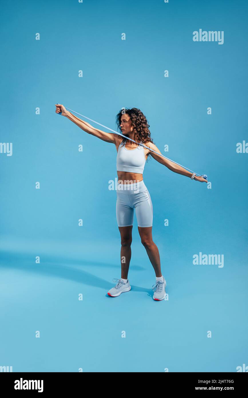 Weibliche Sportbekleidung macht ein Stretching-Workout mit einem Widerstandsband auf blauem Hintergrund Stockfoto