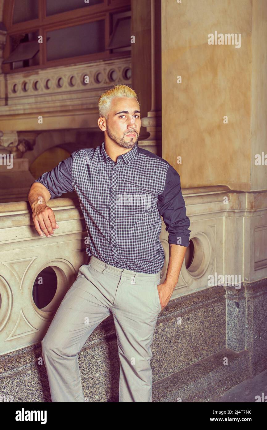 Porträt eines jungen Arbeiters. In einem schwarz gemusterten Hemd, einer gelben Hose, steht ein junger Mann mit Bart, gelben Haaren an einem Geländer auf dem Büro h Stockfoto