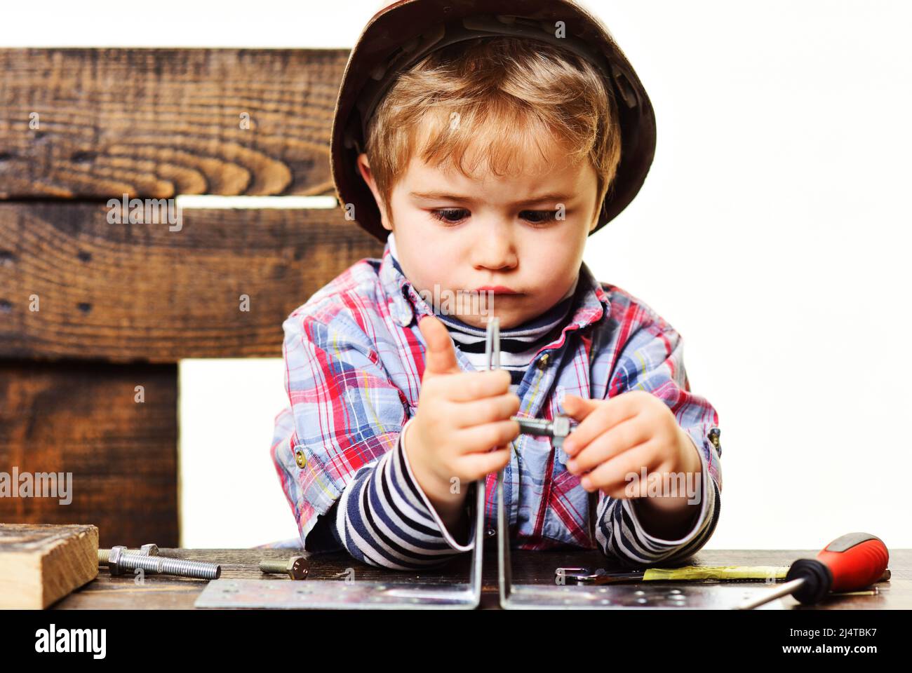 Das Kind verbindet Metallblechteile mit einer Schraube. Reparaturkonzept. Junge in der Werkstatt verbindet Stahlplatte. Stockfoto