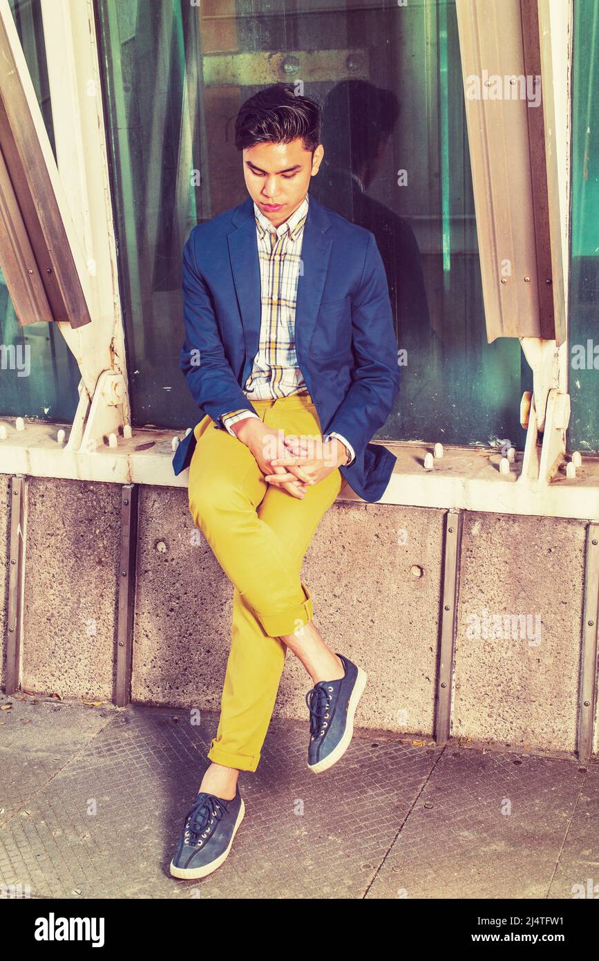 Einsamer Mann. Dressing in blauen Blazer, gemustert unter Verschleiß, gelbe Hosen, Turnschuhe, Hände kreuzen, Beine, sengenden Kopf, ein junger, hübscher Kerl ist Sitti Stockfoto