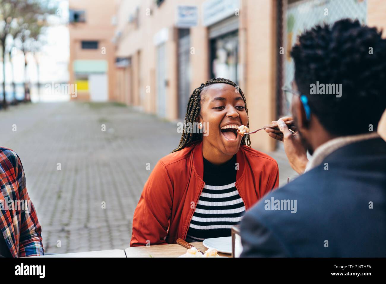 Junge schwarze Frau öffnet ihren Mund, um Essen zu essen, das ihr von ihrem Partner angeboten wird Stockfoto