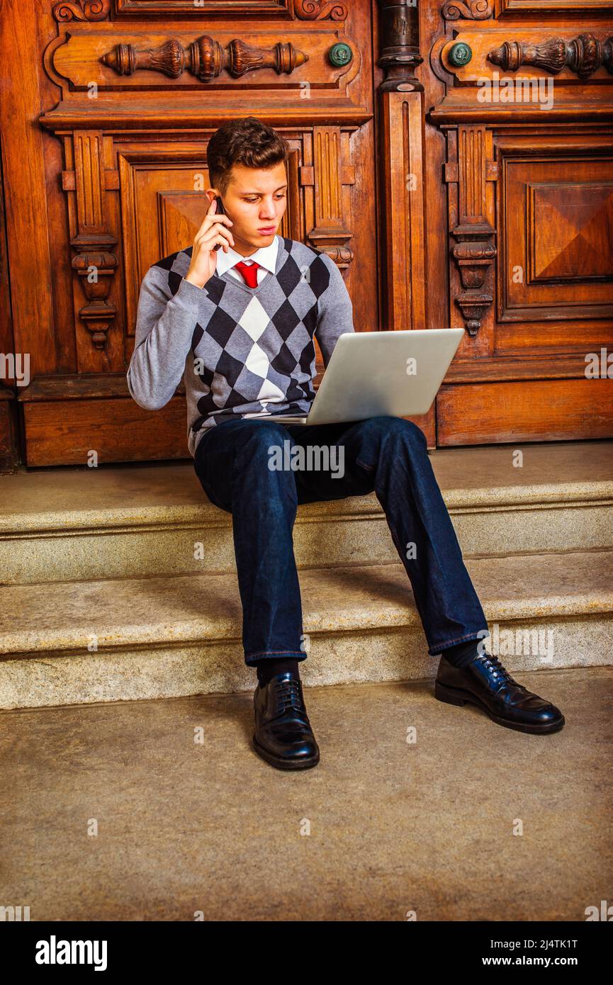 Mann, Der Hart Arbeitet. In einem gemusterten Pullover, einer roten Krawatte,  einer blauen Jeans und Lederschuhen sitzt ein junger Mann auf der Treppe  vor der Bürotür und redet Stockfotografie - Alamy