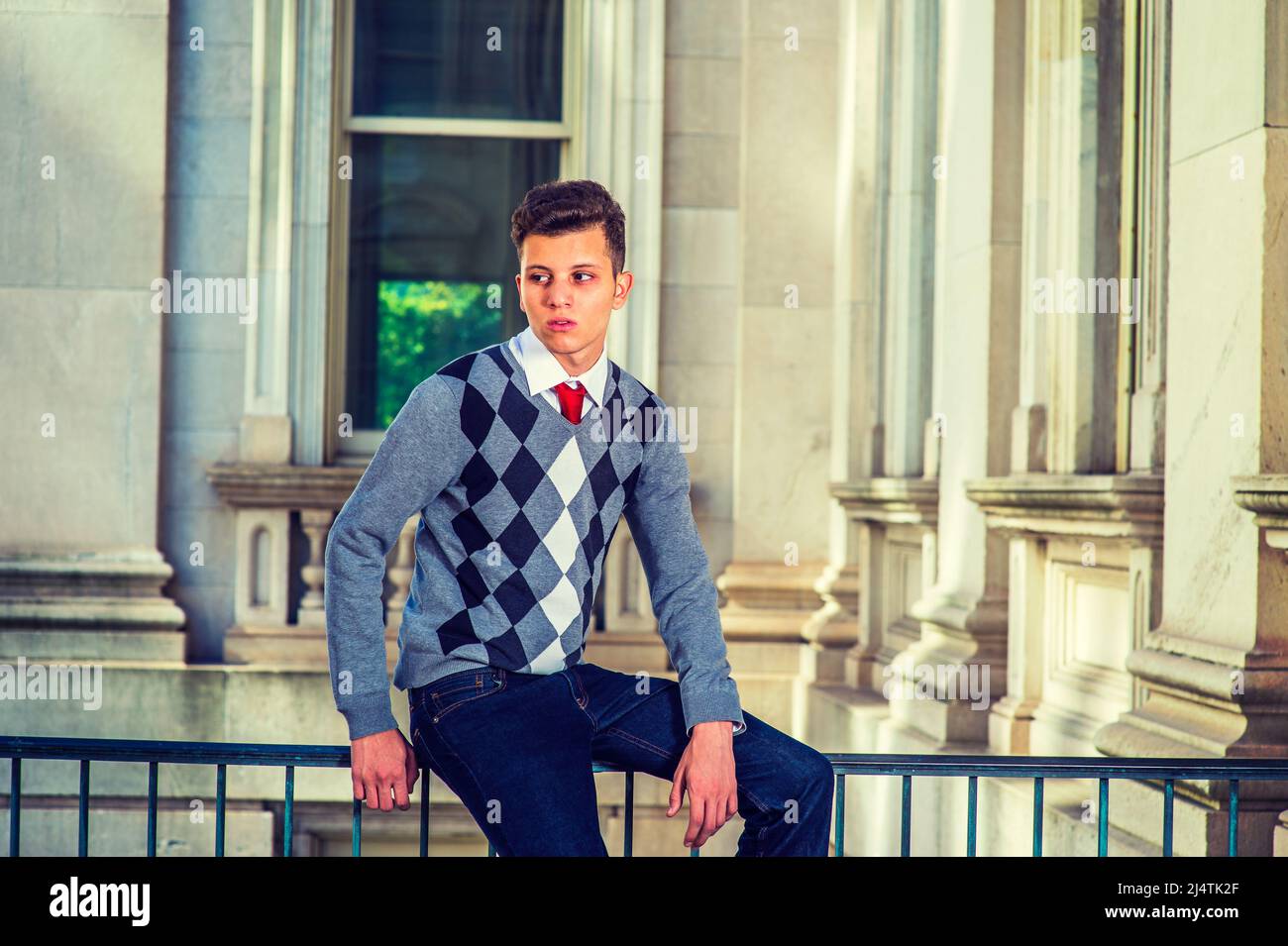 Mann, Der Sich Draußen Entspannt. In einem schwarz-weißen, grau gemusterten Pullover, Jeans, sitzt ein junger, gutaussehender Profi auf einem Geländer in einem Büro BU Stockfoto