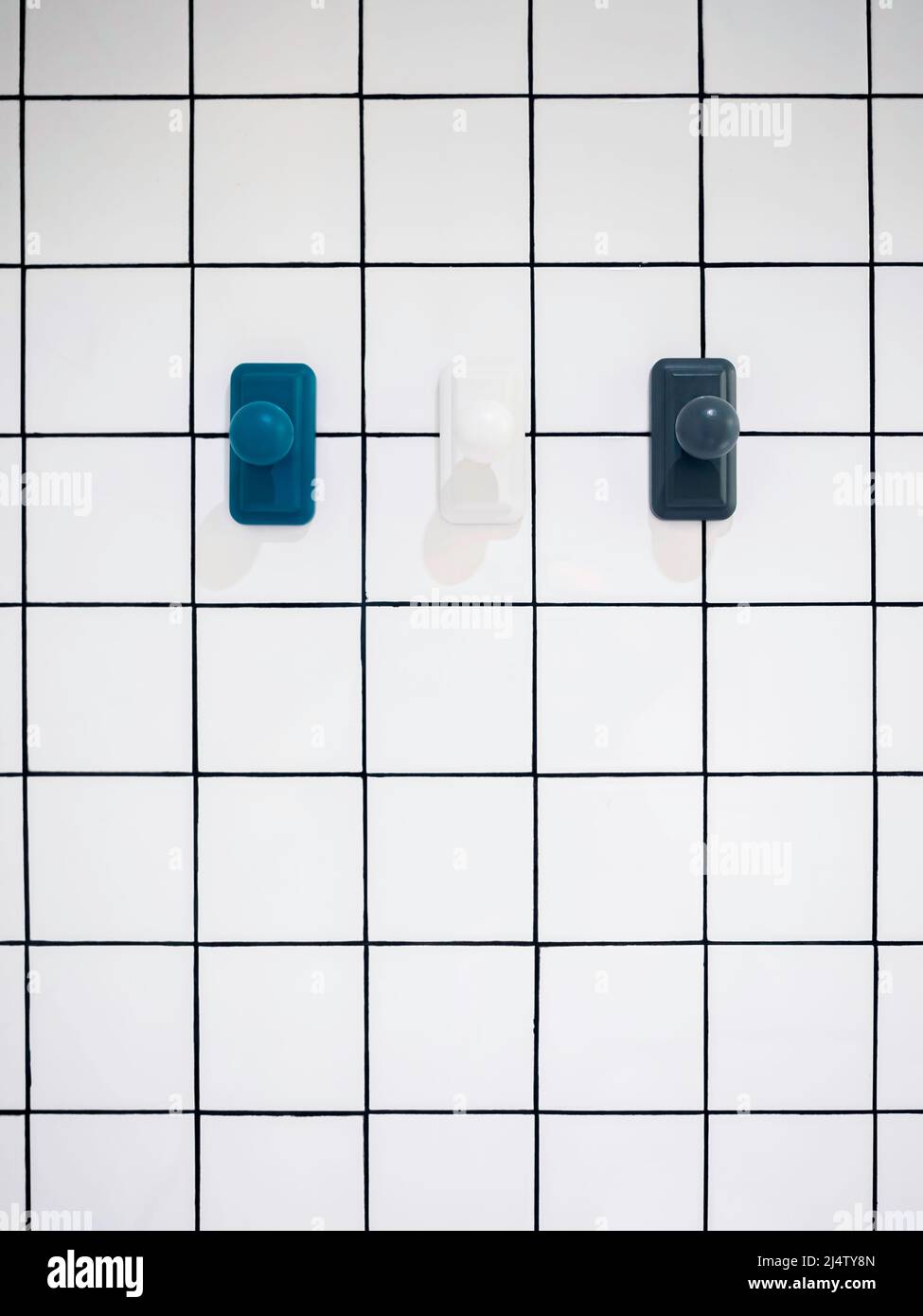 Leere drei moderne Handtuchhaken, blau und weiß hängen auf weißen Gitterwand Badezimmer Hintergrund mit Kopierer Platz, minimalistischen Stil, vertikal. Stockfoto