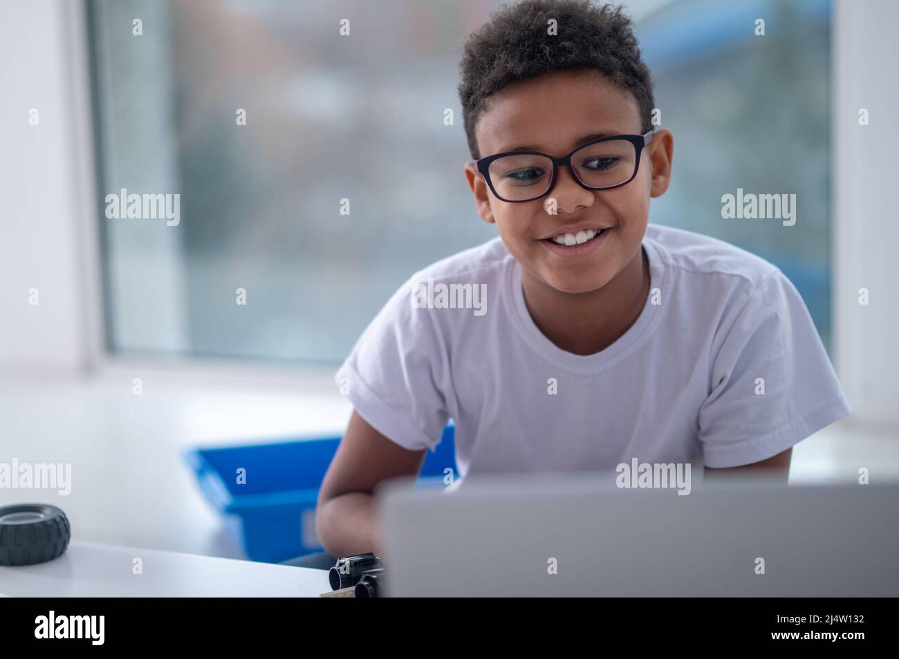Ein lächelnder, dunkelhäutig sitzender Junge am Laptop Stockfoto