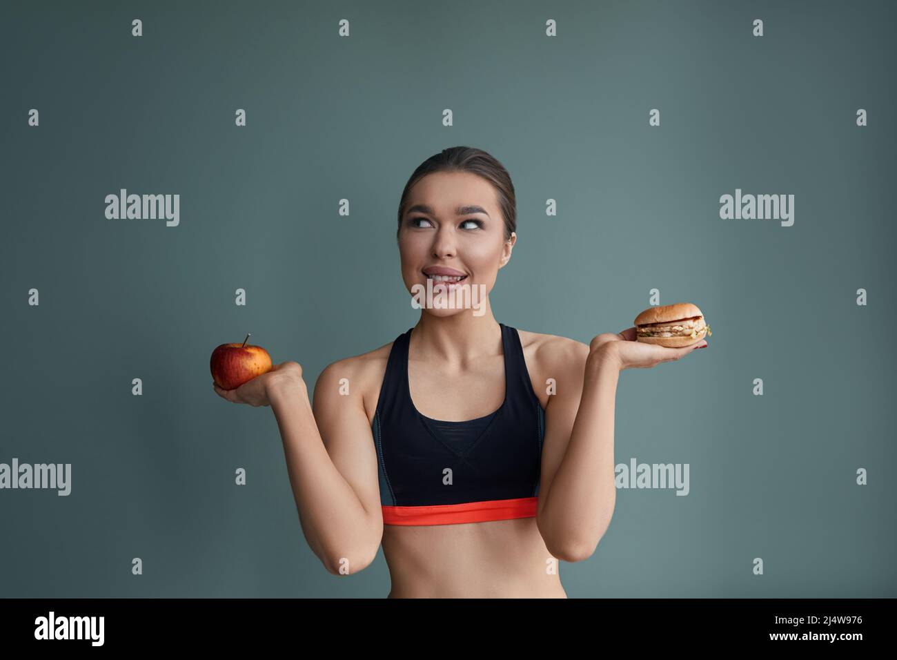 Frau, die zwischen Apfel und Hamburger wählen kann. Diät-Konzept. Gesunde Ernährung. Stockfoto