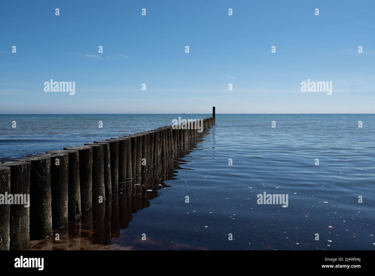 Maritimer Hintergrund, hölzerner Wellenbrecher in ruhiger ostsee vor blauem Himmel Stockfoto