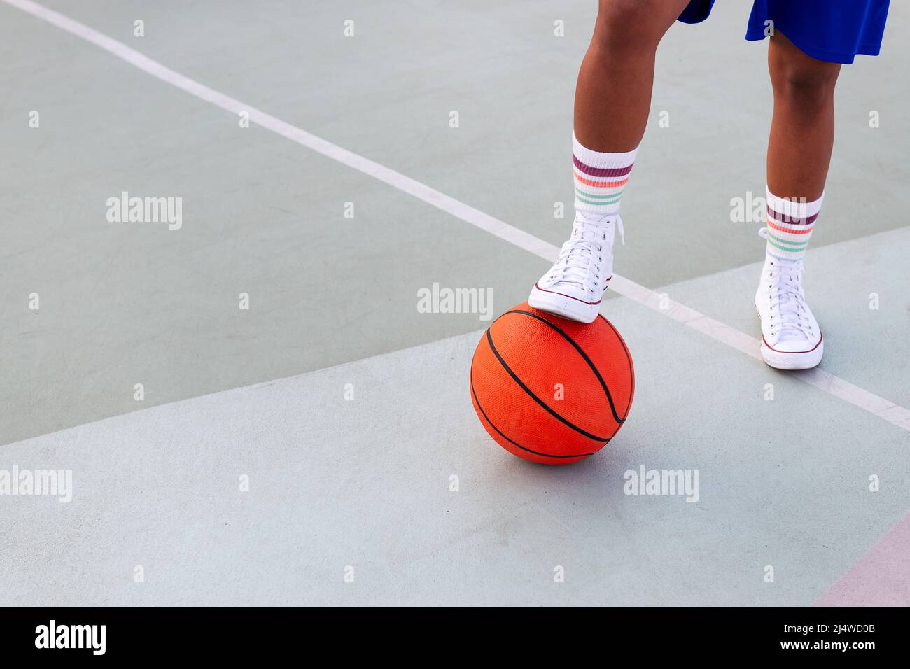 Fuß einer nicht erkennbaren Person, die einen Basketball auf dem Platz hält, Konzept des städtischen Sports auf der Straße, Platz für Text kopieren Stockfoto