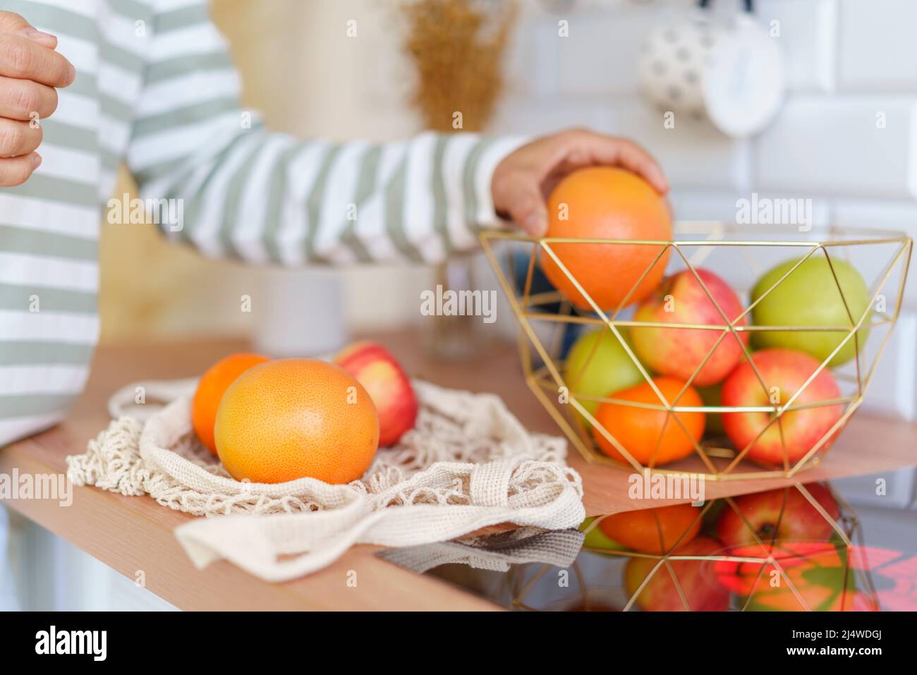 Gesichtslose Person, die einen reifen Apfel aus der Obstschale auf dem Küchentisch ergreift. Sortieren nach dem Lebensmittelgeschäft Stockfoto