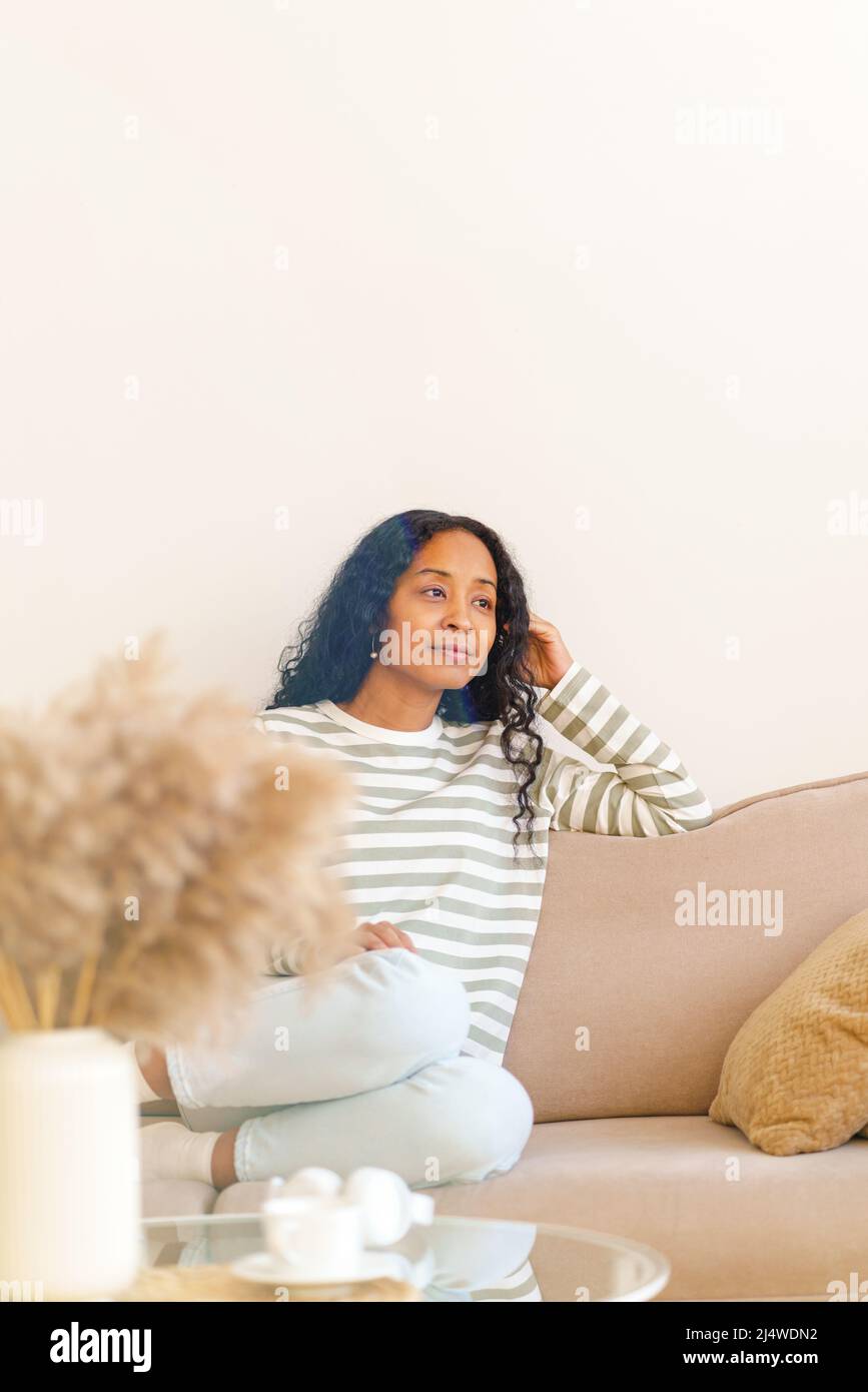 Nachdenkliche afroamerikanische Frau, die im Wohnzimmer auf der Couch sitzt und träumt, selektiver Fokus Stockfoto