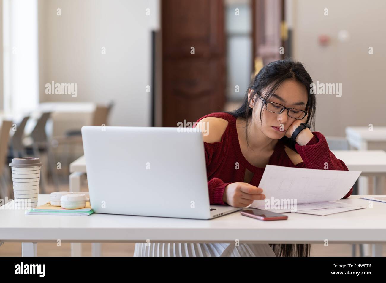 Müde gelangweilt asiatische weibliche Student lesen gedruckte Papiermaterialien während des Studiums in der Bibliothek Stockfoto