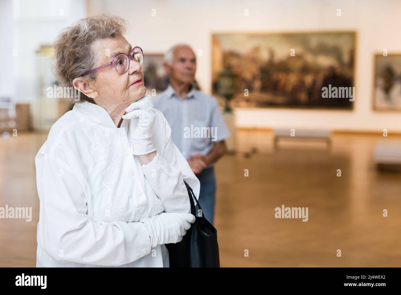 Reife Frau untersucht Gemälde in einer Ausstellung in der Halle eines Kunstmuseums Stockfoto