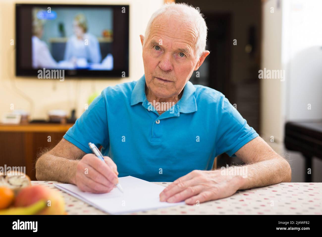 Fokussierter älterer Mann, der zu Hause sitzt und Papiere liest und unterschreibt Stockfoto