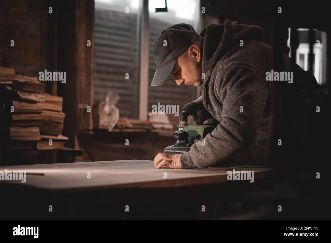 Ein Zimmermann arbeitet in einer Werkstatt. Tischlerschleifer, Möbelherstellung. Ein Tischler mahlen ein Holzteil mit einem elektrischen Schleifer. Stockfoto