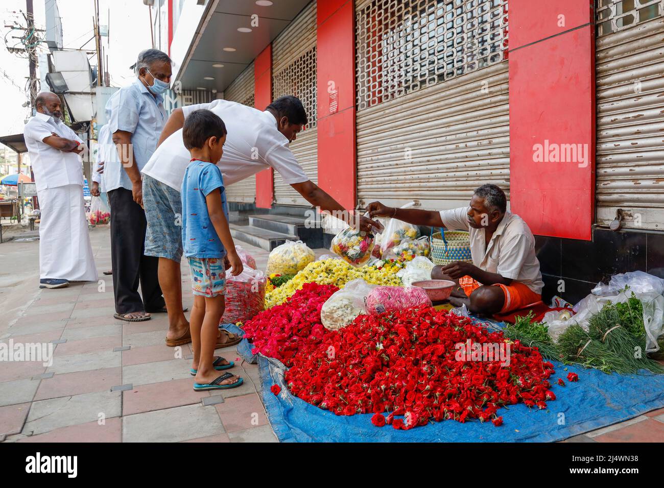 Mann, der auf dem Bürgersteig sitzt und die Blumenköpfe nach Gewicht in Trichy, Tamil Nadu, Indien verkauft Stockfoto