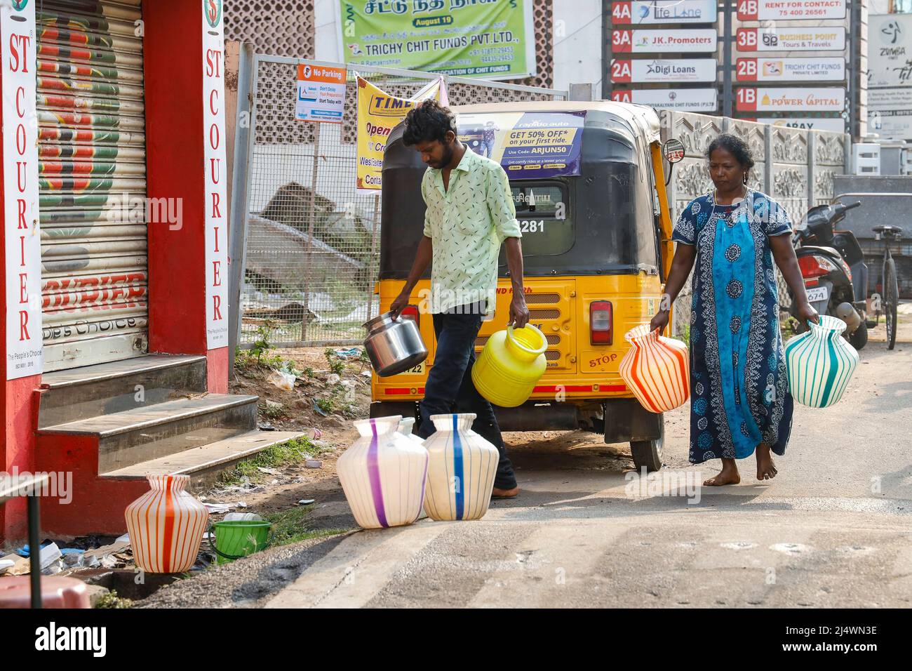 Mann und Frau, die zu einem öffentlichen Brunnen gehen, um Kannen mit Wasser zu füllen, Trichy, Tamil Nadu, Indien. Stockfoto