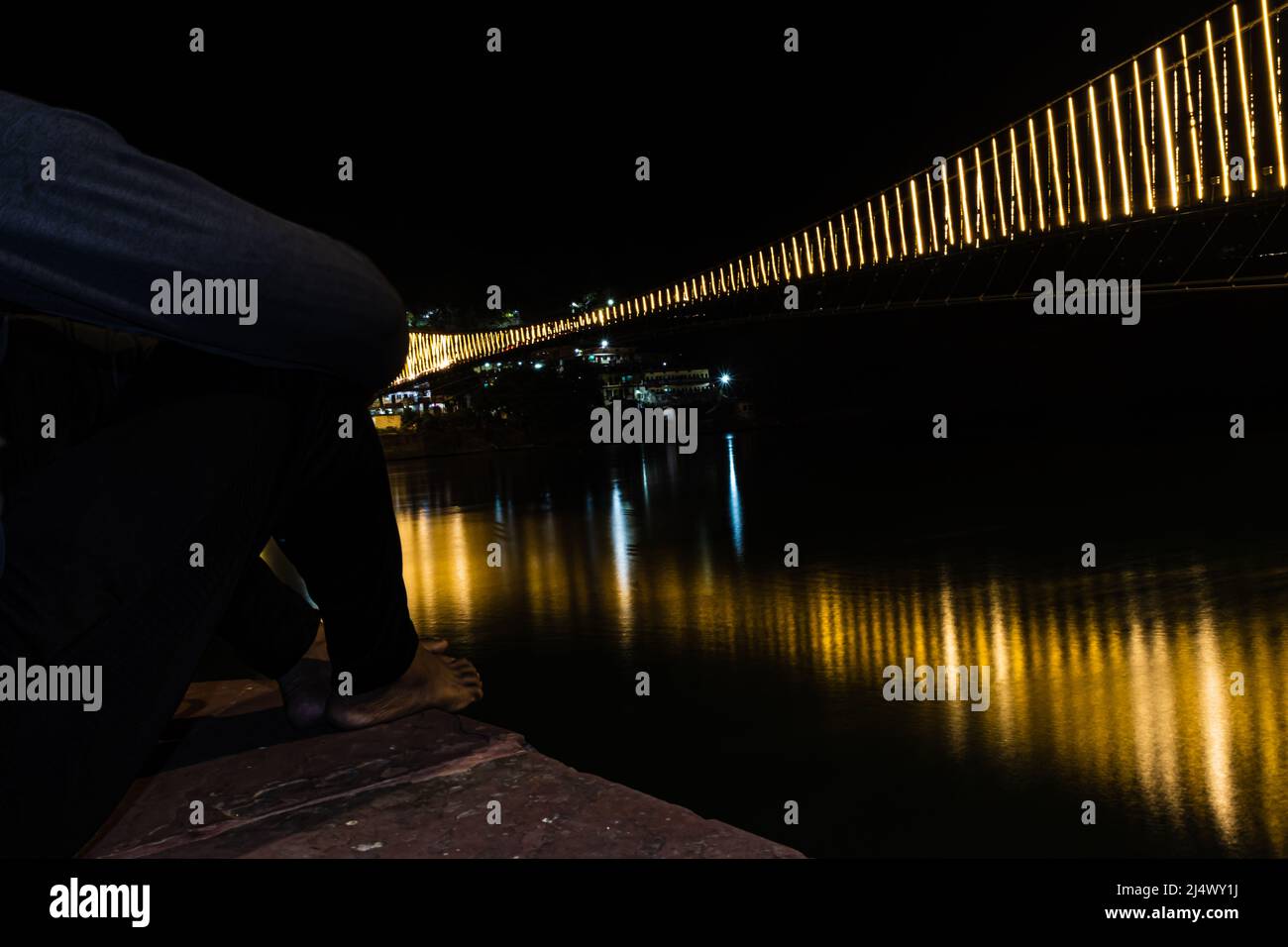 Mann beobachten Eisen Hängebrücke mit Fähre Lichter mit Wasser Reflexion Bild beleuchtet wird in rishikesh uttrakhand indien aufgenommen. Stockfoto
