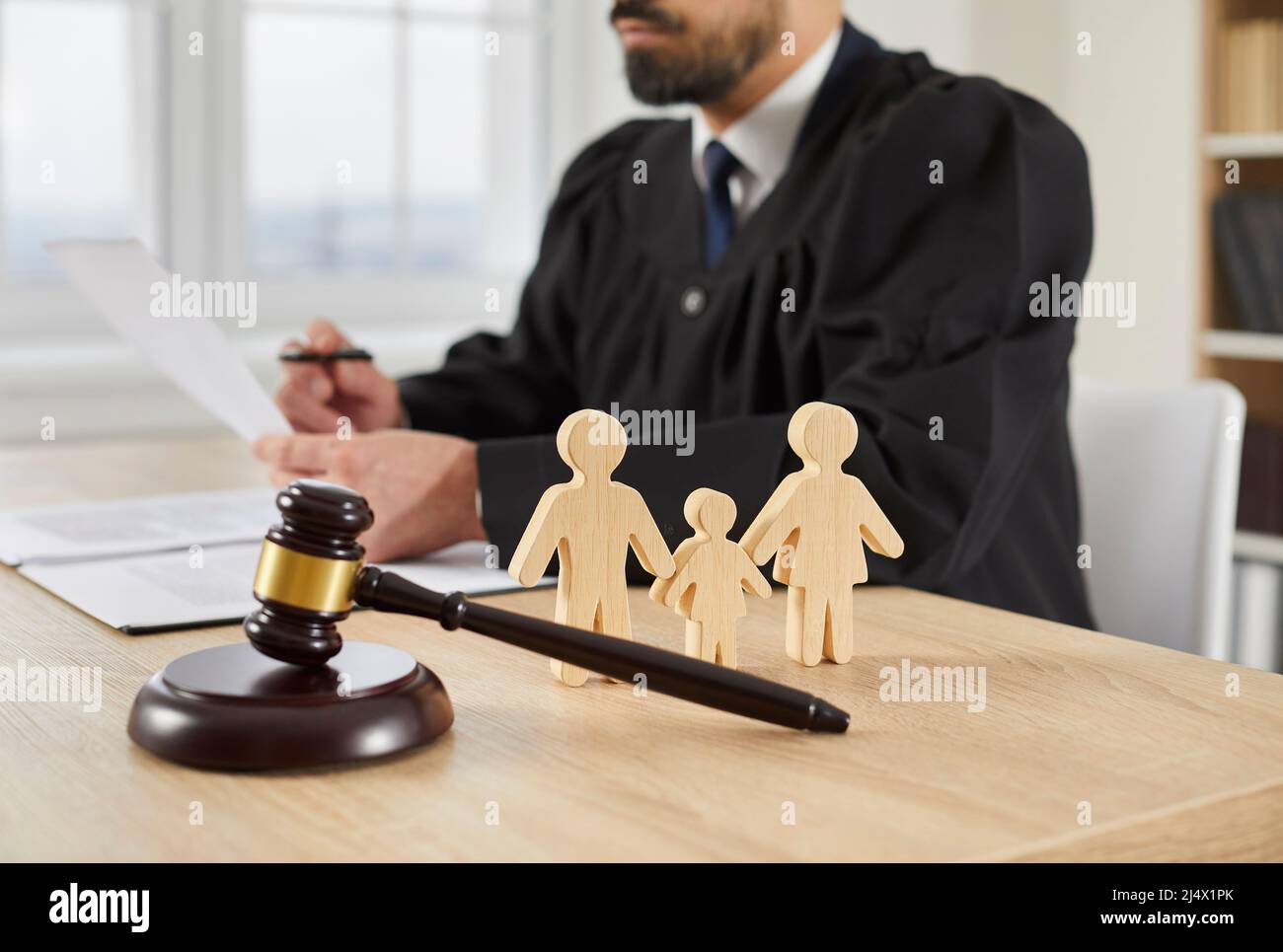 Gavel und kleine Familienfiguren auf dem Tisch im Gerichtssaal, mit Richter im Hintergrund Stockfoto