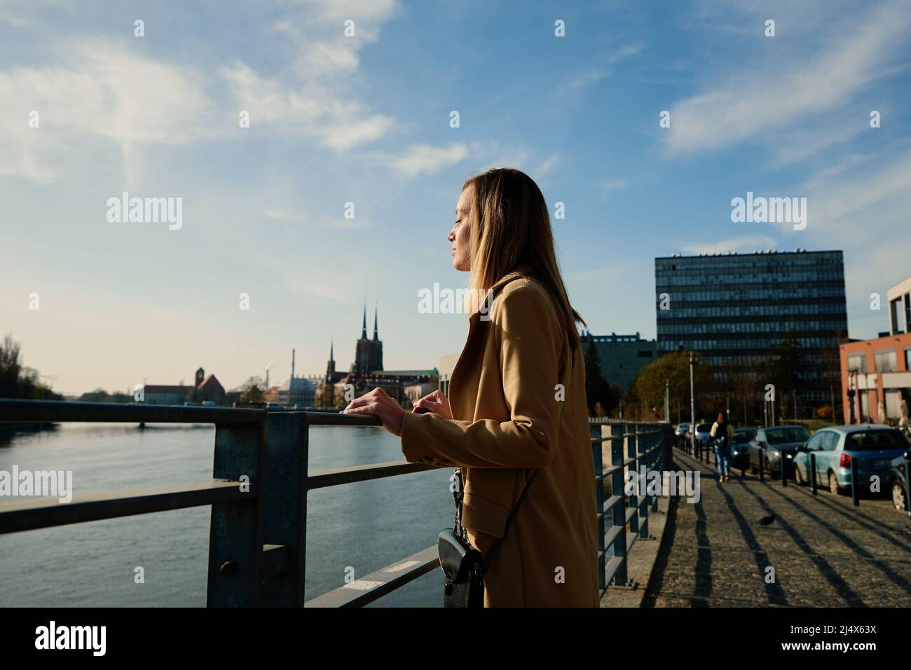 Tausendjährige kaukasische Frau, die am Flussufer steht und einen sonnigen Tag genießen kann, weibliche Touristen, die einen stilvollen Graben in der europäischen Stadtstraße trägt Stockfoto