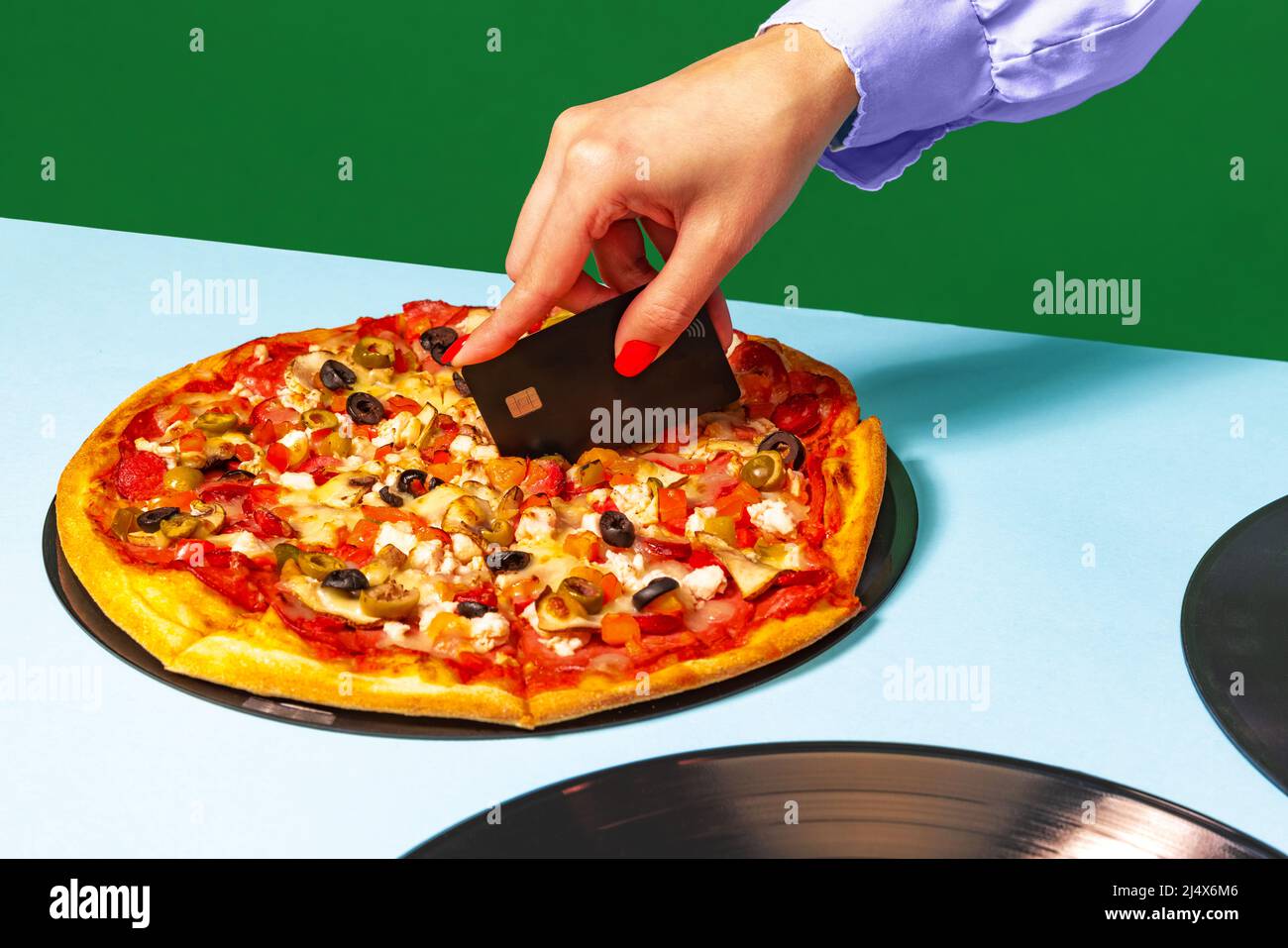 Kreative Pizza schneiden. Weibliche Hände mit italienischer Pizza liegen auf Vinylscheiben auf heller Tischdecke isoliert auf grünem Hintergrund. Vintage-Retro-Style Stockfoto