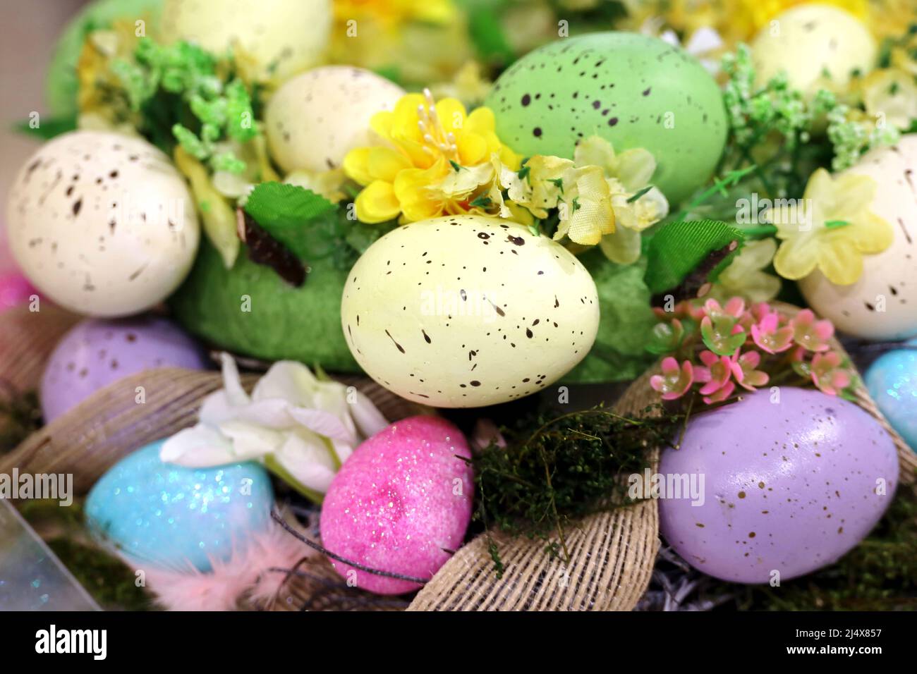 Ostereier und künstliche Blumen im Weidenkorb. Bunte Dekorationen, festlicher Hintergrund Stockfoto