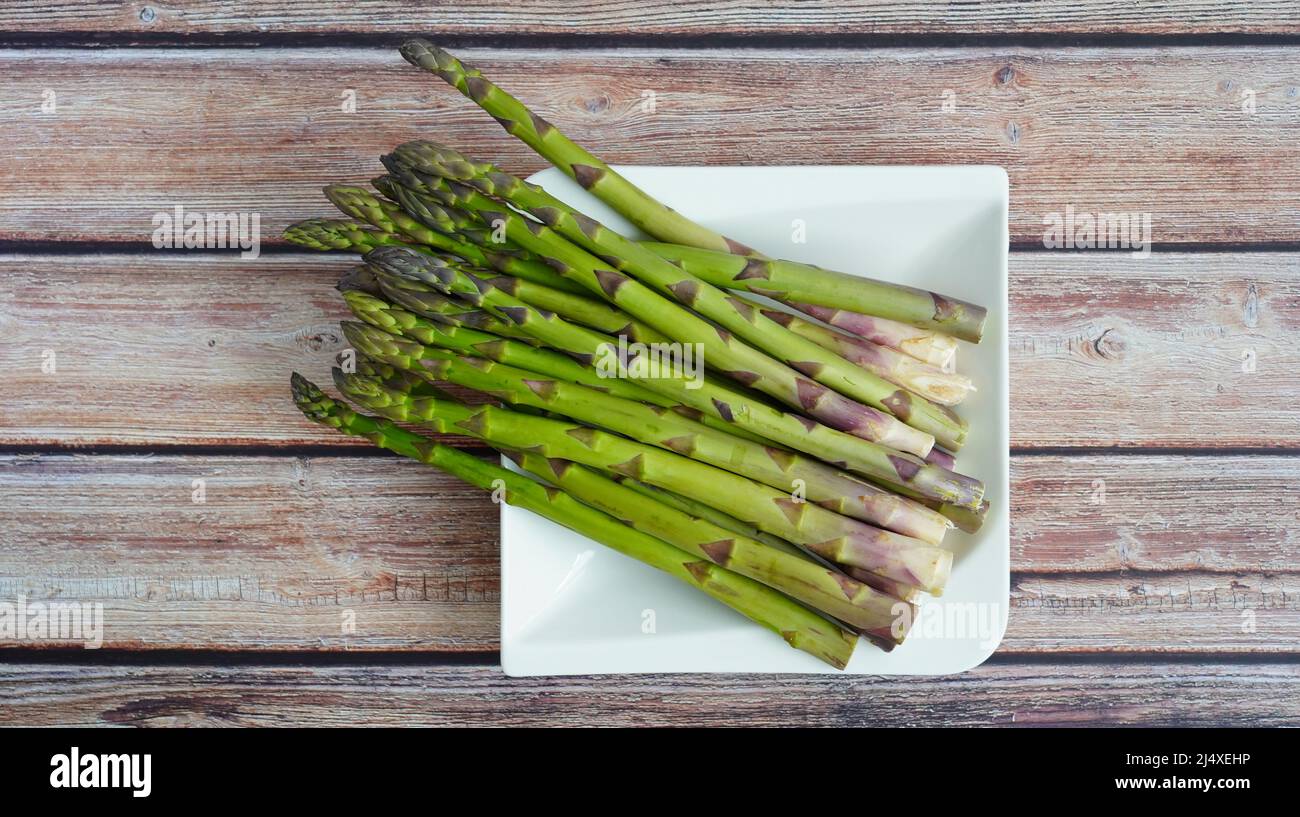 Grüner Bio-Spargel auf einem weißen Teller mit rustikalem Holztischhintergrund. Stockfoto