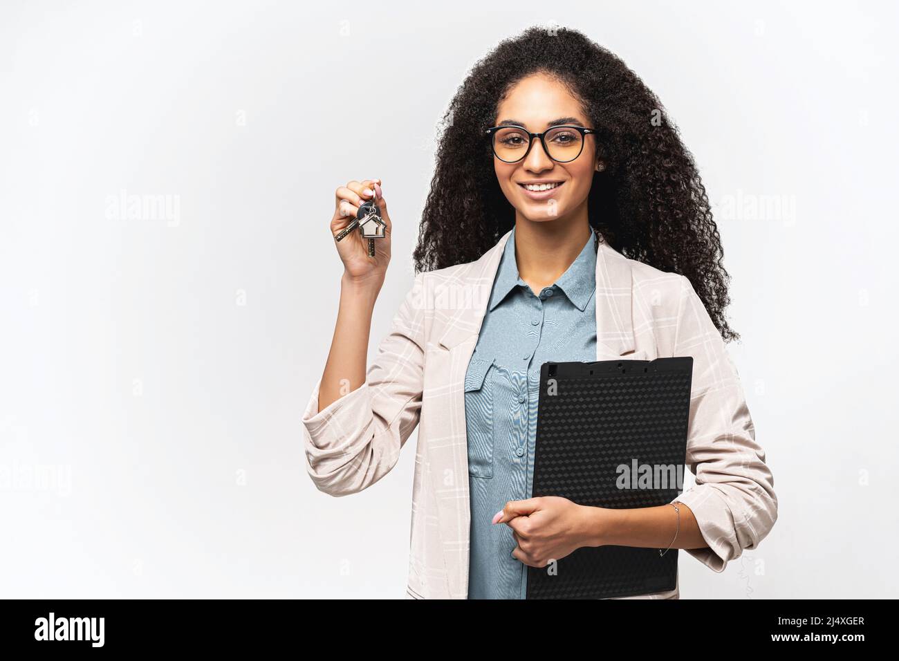 Lächelnd fröhlich multirassischen Immobilienmakler hält Zwischenablage und zeigt Schlüssel, charmante afroamerikanische Frau smart casual wear hält Schlüssel isoliert auf weiß Stockfoto