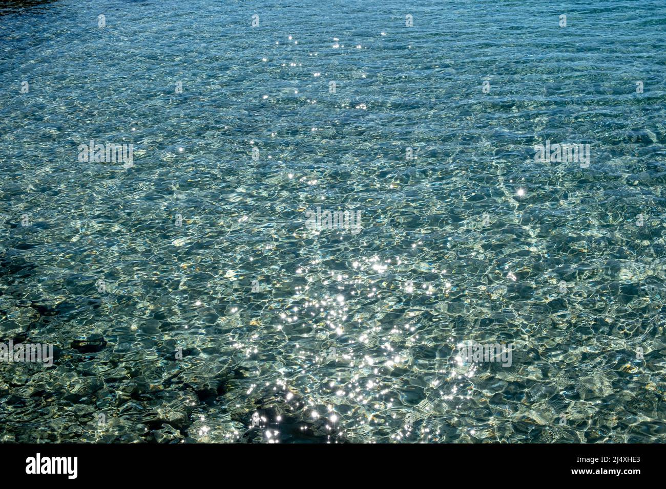 Meerwasseroberfläche mit glänzenden Reflexionen Hintergrund. Klares, flaches, blau schimmerndes Wasser und felsiger Meeresboden, oben. Ägäis Griechenland Stockfoto