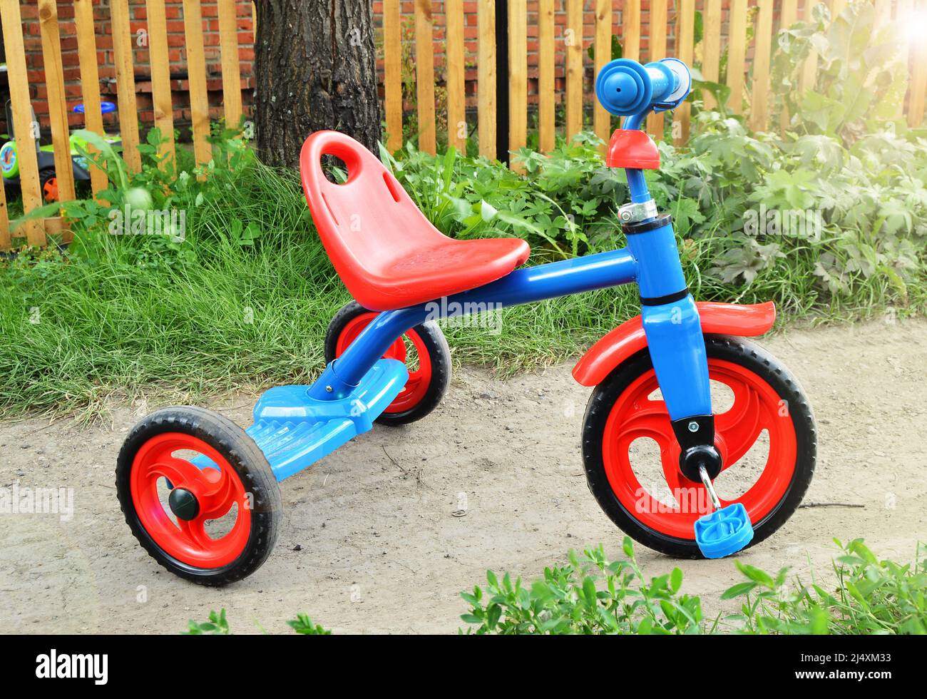 Buntes neues Dreirad Kinderfahrrad im Freien an einem sonnigen Sommertag vor dem Hintergrund von Gras und Straße, das Konzept der Sicherheit und des Schutzes Stockfoto