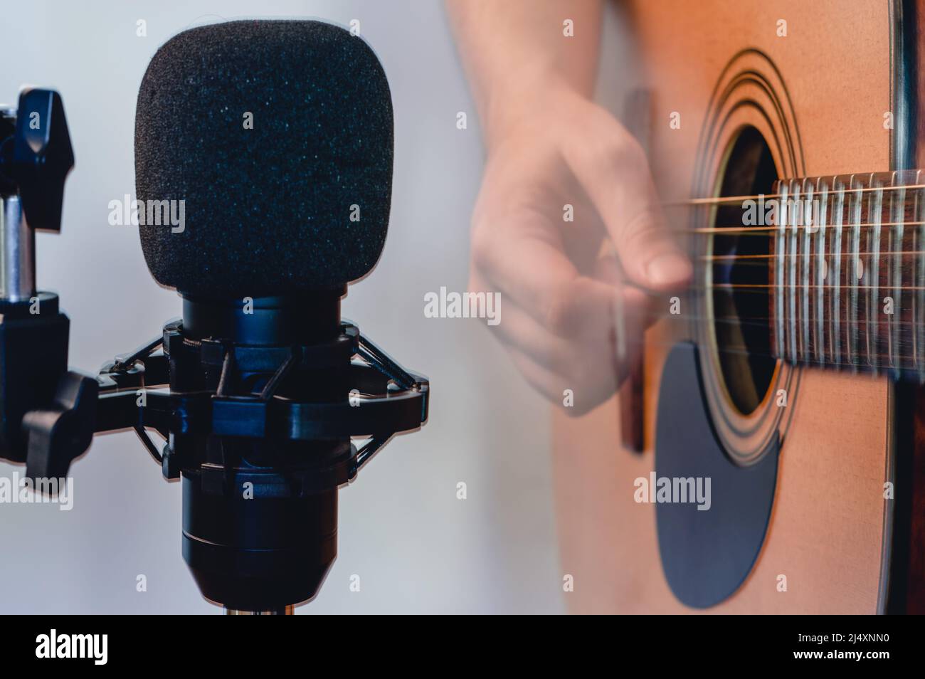 Nahaufnahme Kondensatormikrofon mit verschwommenem Mann, der akustische Gitarre mit Plektrum im Hintergrund mit Kopierraum spielt, Musik im Studio mit aufnimmt Stockfoto
