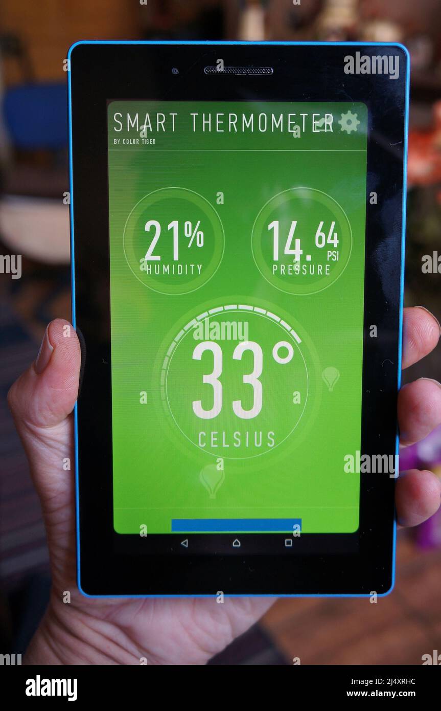 Hand mit einem Tablet-PC, der in der Wetter-App 33c Temperatur und Luftfeuchtigkeit anzeigt Stockfoto