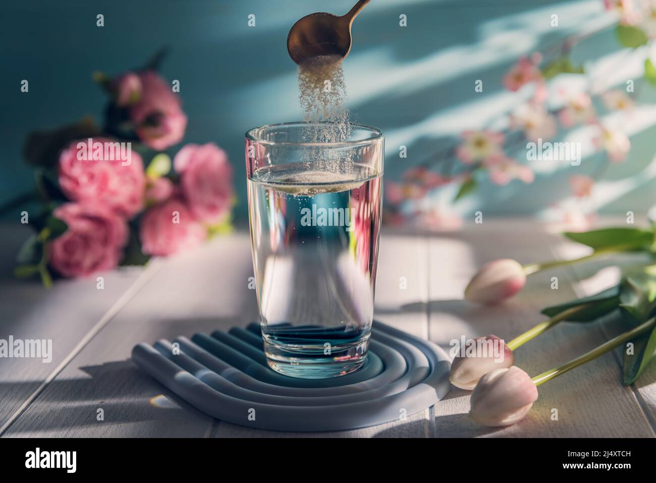 Kollagenpulver wird mit einem Löffel in ein Glas Wasser gegeben Stockfoto