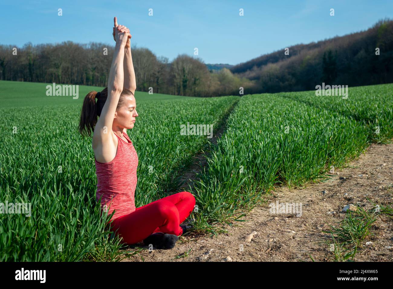 Sportliche Frau, die auf einem grünen Feld sitzt und Yoga praktiziert und meditiert. Stockfoto
