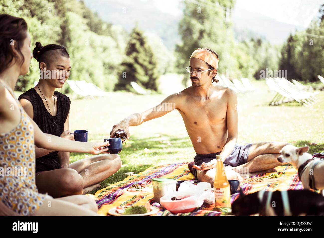 Mann gießt Getränke für zwei Frauen beim Sommerpicknick mit Hunden in frankreich Stockfoto