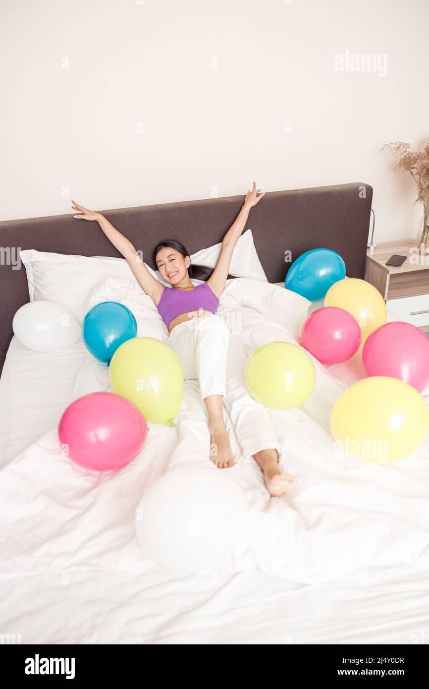 Fröhliche Frau, die zu Hause mit bunten Ballons im Bett liegt Stockfoto