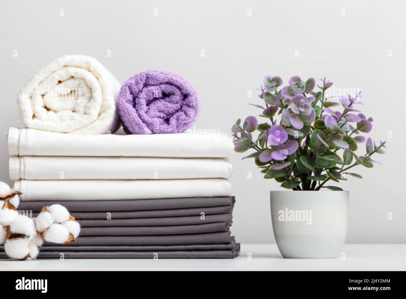 Stapel Bettwäsche, Bettwäsche und Handtücher mit Baumwollzweig und Topfpflanze auf dem Tisch Stockfoto