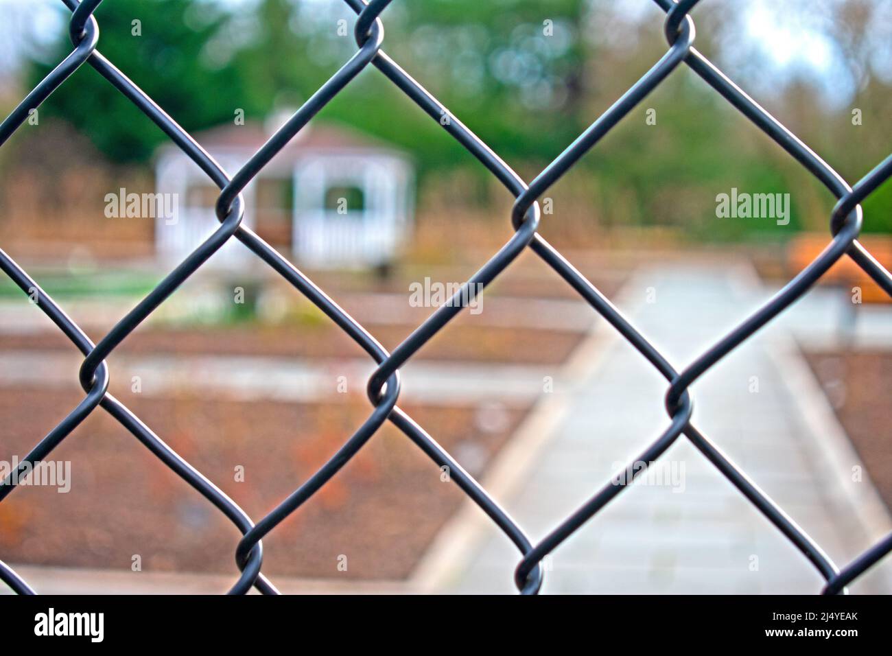 Rosengarten im Colonial Park, Franklin, New Jersey, der im frühen Frühjahr durch einen Kettengliederzaun mit selektivem Fokus auf den Zaun -02 betrachtet wird Stockfoto
