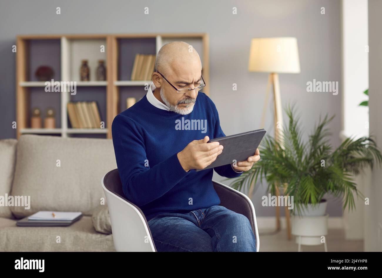 Seriös älterer Mann in Brille sitzt auf einem Stuhl und mit seinem modernen digitalen Tablet Stockfoto