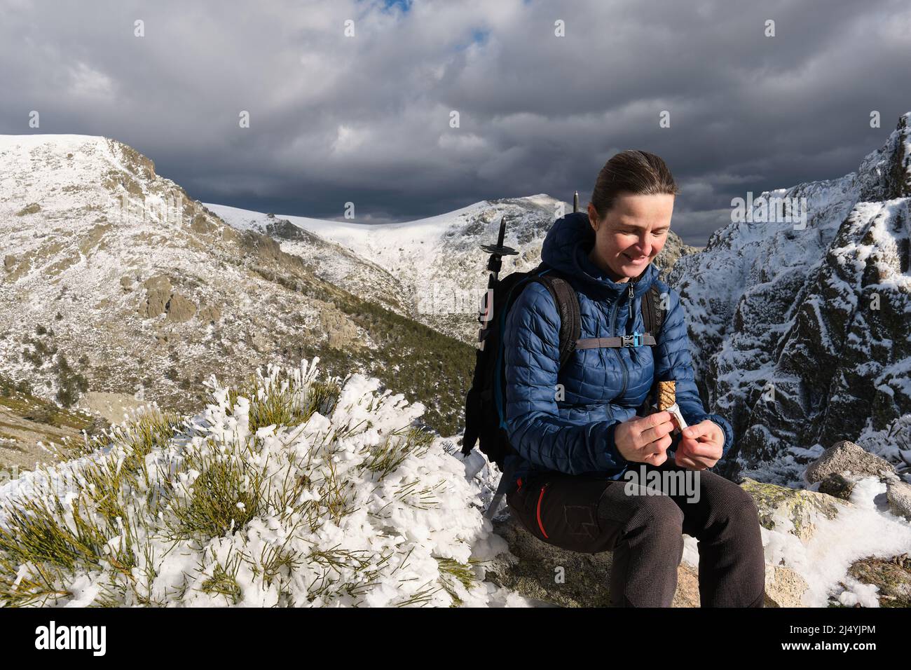 Eine gute Backpacker-Frau, die einen Snack isst, während sie auf einem verschneiten Berg sitzt Stockfoto